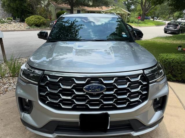 Clean silver hood and chrome grille of the 2025 Ford Explorer Platinum reflecting the trees above