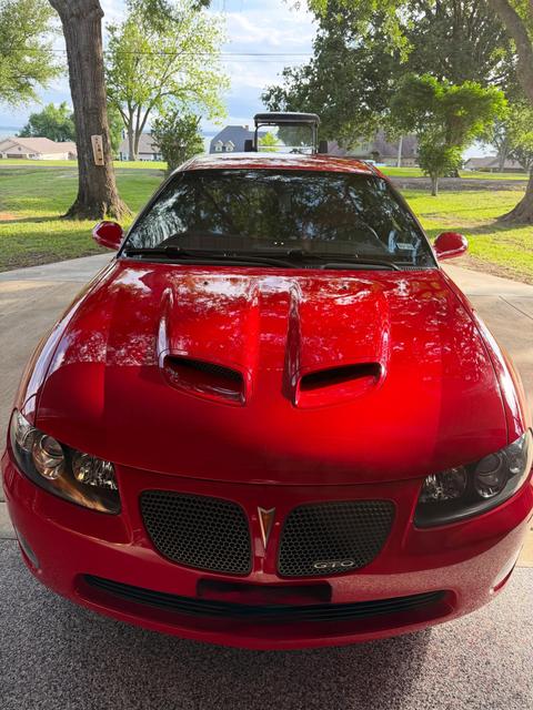 Head-on view of the red Pontiac GTO with trees reflected across the clean hood and its twin scoops