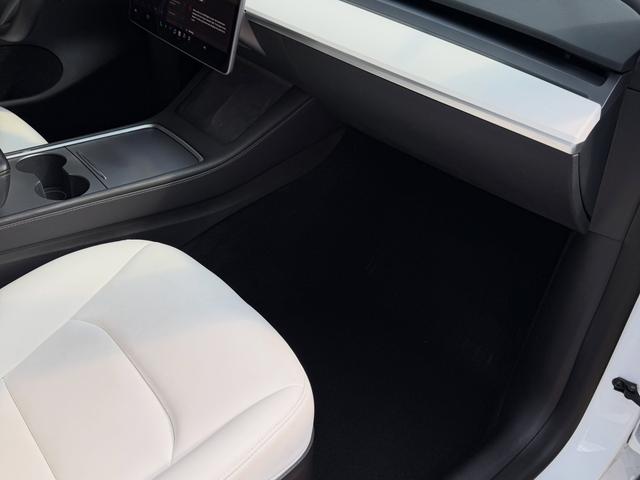 Passenger footwell and center console of the Model Y after a deep vacuum, with clean black carpet and white dash trim
